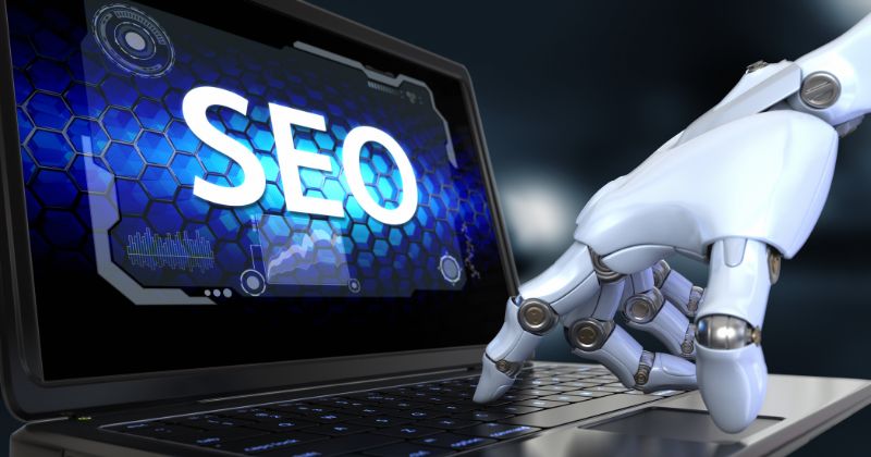 Alt Text: SEO displayed on a laptop screen, with a robotic AI hand operating the laptop keyboard
