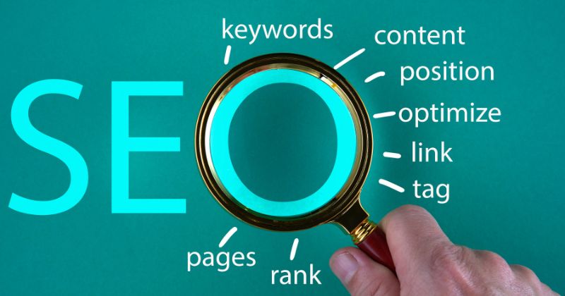 Magnifying glass emphasises 'O' in SEO, surrounded by SEO-related keywords