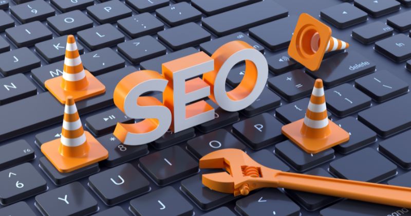 SEO word in orange and white on keyboard tiles, surrounded by a cone road and screws.